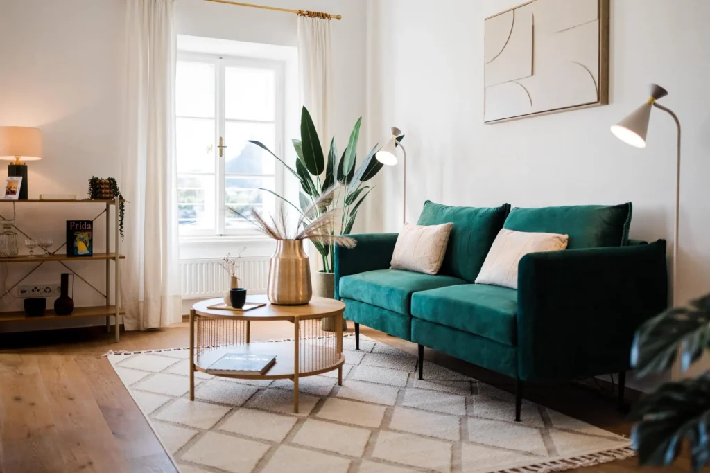 Modern eingerichtetes Wohnzimmer mit einem smaragdgrünen Samtsofa, Holzboden und hellem Interieur als Beispiel für gehobenen Wohnstandard bei der Immobiliensuche und im Kauf-FAQ.