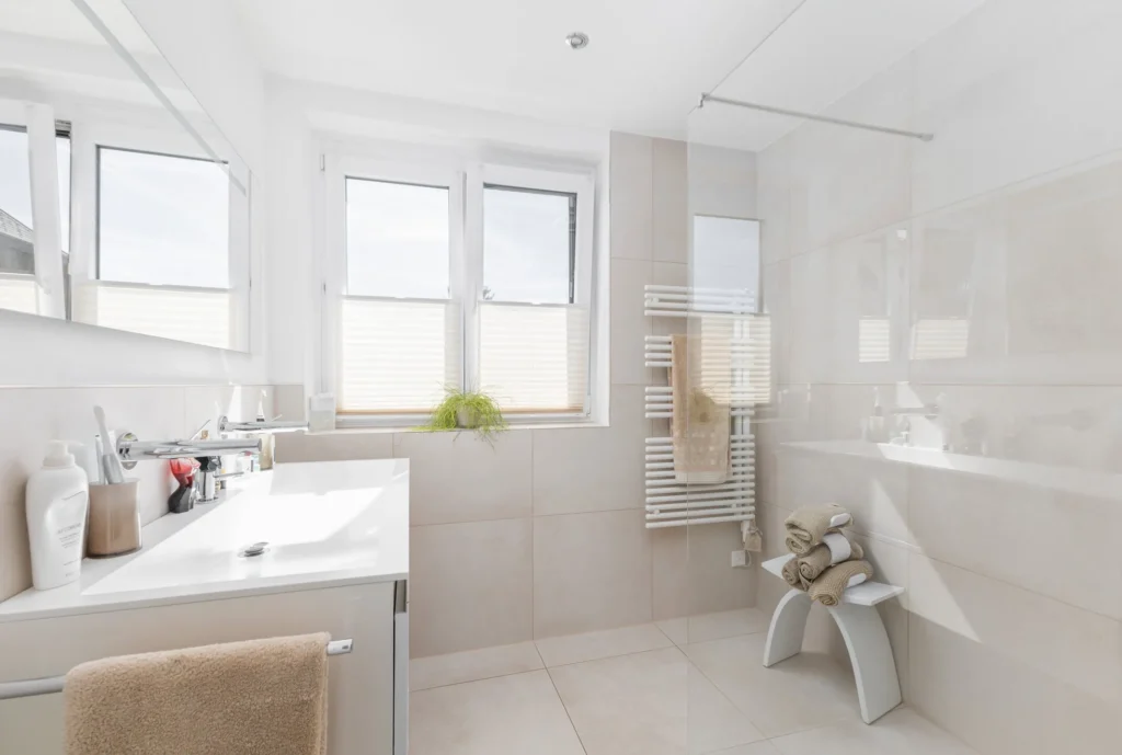 Ein helles, modern gestaltetes und verkaufsoptimiertes (homestaging) Badezimmer mit Doppel-Waschtisch, Dusche und viel Tageslicht. Es dient als visuelles Beispiel für die perfekte Vorbereitung einer Immobilie für den Verkauf und veranschaulicht Themen der Hausverkauf-FAQ.