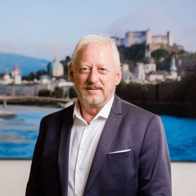 Portrait von Günter Penninger - konzessionierter Immobilienmakler & Firmengründer - mit einem Foto der Stadt Salzburg im Hintergrund.